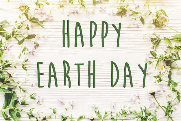 Happy earth day tekstteken op mooie lila en madeliefjebloemen op rustieke witte houten achtergrond bovenaanzicht wenskaart milieuconcept earth day save environment eco