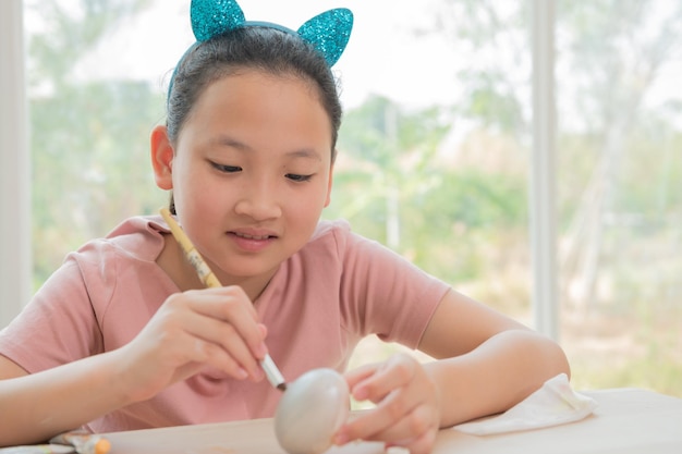 Photo happy easter a beautiful child girl painting easter eggs happy family preparing for easter cute little child girl wearing bunny ears on easter day