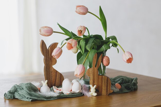 Happy easter beautiful tulips eggs and bunny decoration on wooden table modern farmhouse easter decor stylish handmade egg holder natural eggs pink tulips bouquet and rustic bunnies