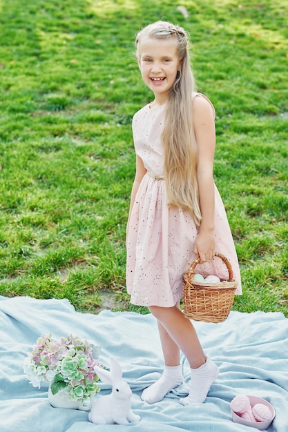 Happy Easter bunny. Child having fun outdoor. Kid playing with eggs and rabbit on green grass.