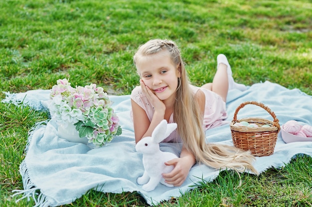 Happy Easter bunny. Child having fun outdoor. Kid playing with eggs and rabbit on green grass.