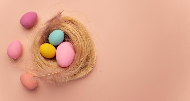 Фото Счастливая пасхальная открытка окрашена в желтые розовые голубые пасхальные яйца на бежевом фоне гнезда сверху.