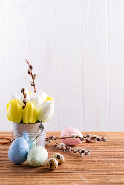 Happy Easter card with fresh spring tulips flowers in a bucket and handmade painted eggs on a wooden table.