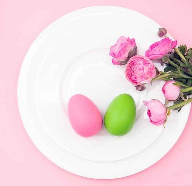 Happy Easter celebration table Easter eggs and flower decoration on plates pink background