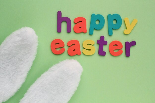 Happy Easter colored lettering and white bunny fur ears on green background. Holiday spring composit