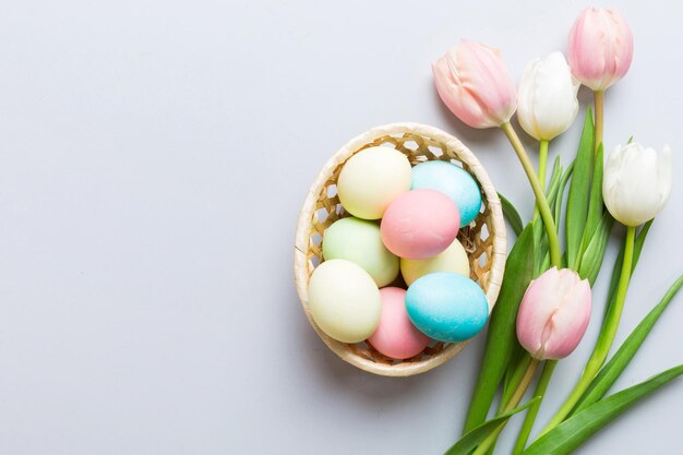 Happy Easter composition Easter eggs in basket on colored table with yellow Tulips Natural dyed colorful eggs background top view with copy space