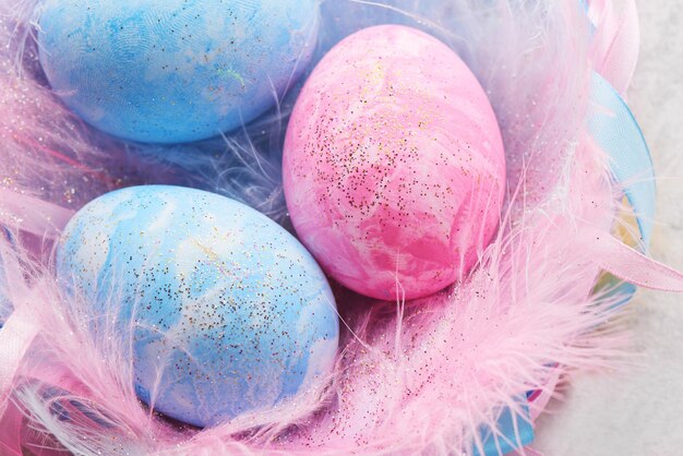 Happy easter concept. Pink and blue painted chicken eggs decorated with feathers and ribbons nest on light background close up with copy space