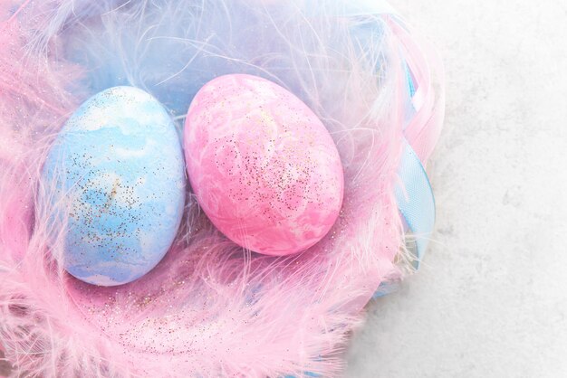 Happy easter concept. Pink and blue painted chicken eggs decorated with feathers and ribbons nest on light background close up with copy space