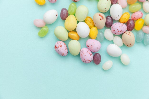 Концепция счастливой Пасхи. Подготовка к празднику. Пасхальные конфеты, шоколадные яйца и мармеладные конфеты, изолированные на модном пастельно-голубом фоне. Простой минимализм с плоским видом сверху.