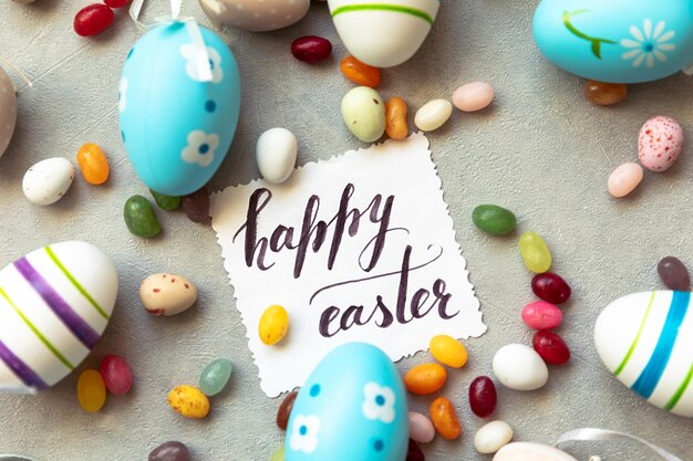 Happy Easter concept Preparation for holiday Easter eggs Inscription HAPPY EASTER letters candy chocolate eggs and jellybean sweets on concrete stone grey background Flat lay top view copy space