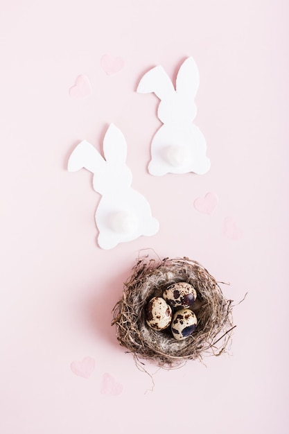 Happy easter couple of white rabbits and quail eggs in nest on pink background top and verical view