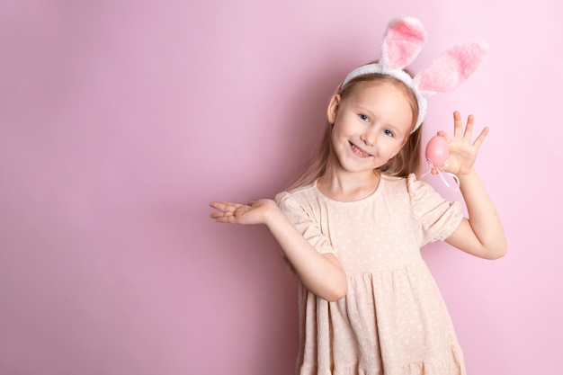 Happy Easter A cute girl with rabbit ears holds colored eggs in her hands and smiles cheerfully pink background Space for text High quality photo