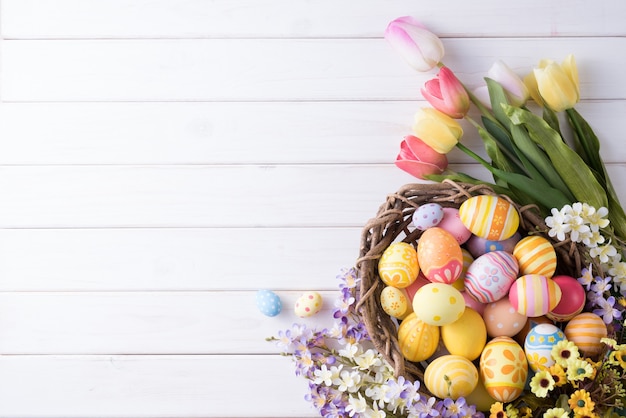 Happy Easter day colorful eggs in nest and flower decoration on white wood