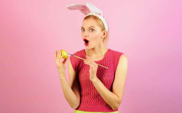 Happy easter day surprised woman in bunny ears painting egg for easter rabbit girl with yellow egg