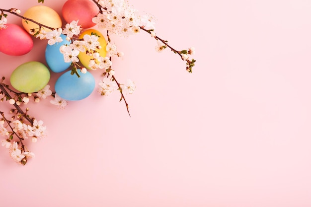 Happy Easter Dyed Easter eggs on rustic table with cherry blossom tree branch on pink background Easter holiday card background with copy space Top view