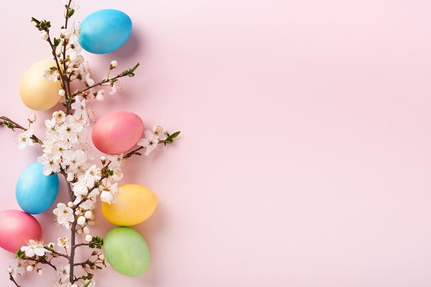 Foto buona pasqua uova di pasqua tinte su tavola rustica con ramo di albero di fiori di ciliegio su sfondo rosa sfondo della carta vacanze di pasqua con spazio per la copia vista dall'alto