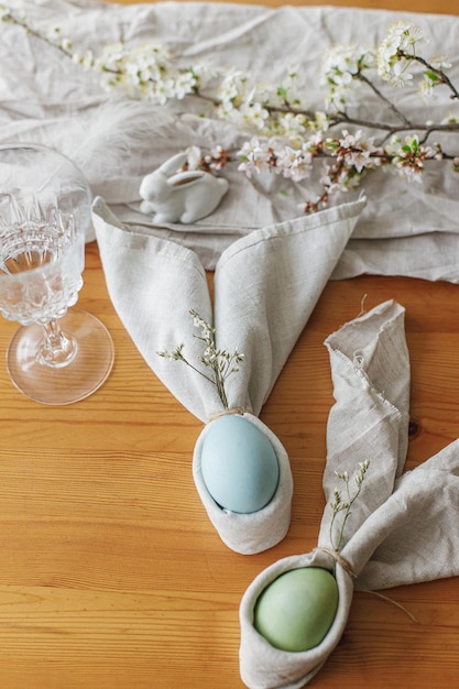 Happy Easter Easter eggs in bunny napkins on wooden table with cutlery bunny flowers top view