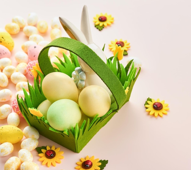 Happy Easter Easter eggs and rabbit in green basket on pink background with white and yellow roses Spring Happy Easter holiday card Easter background with copy space Top view