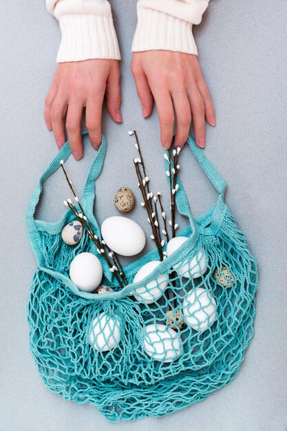 Happy easter female hands hold a blue string bag with chicken and quail eggs