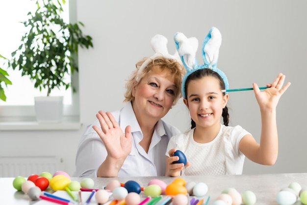 Buona pasqua. una nonna e sua nipote dipingono le uova di pasqua. famiglia felice che si prepara per la pasqua. bambina sveglia che indossa le orecchie da coniglio il giorno di pasqua.