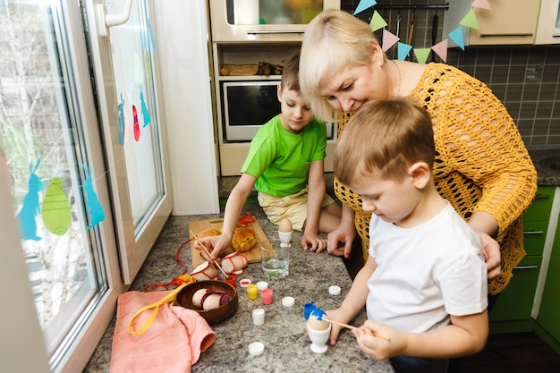 Happy easter. A grandmother and her grandsons painting Easter eggs. Happy family preparing for Easter at home