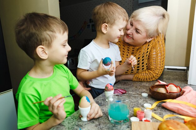 Happy easter. A grandmother and her grandsons painting Easter eggs. Happy family preparing for Easter at home