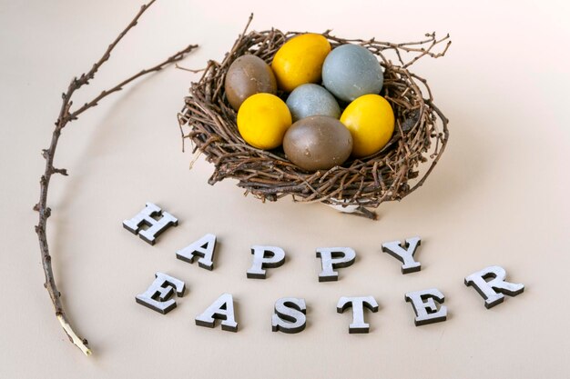 Happy easter lettering branch and colorful Easter eggs in birds nest on gray background