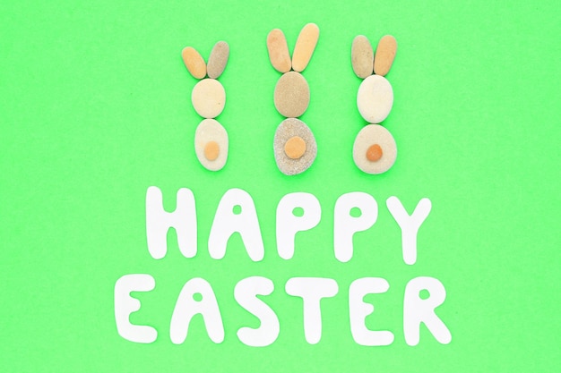 Happy Easter lettering and bunnies from pebbles on green background. Flatlay postcard creative conce