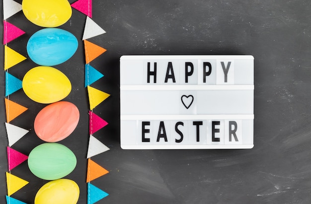 Happy easter lettering on white board with colorful painted eggs and felt garland on chalk board