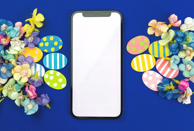 Happy Easter mockup with smartphone, blank white screen with copy space, painted easter eggs and spring flowers