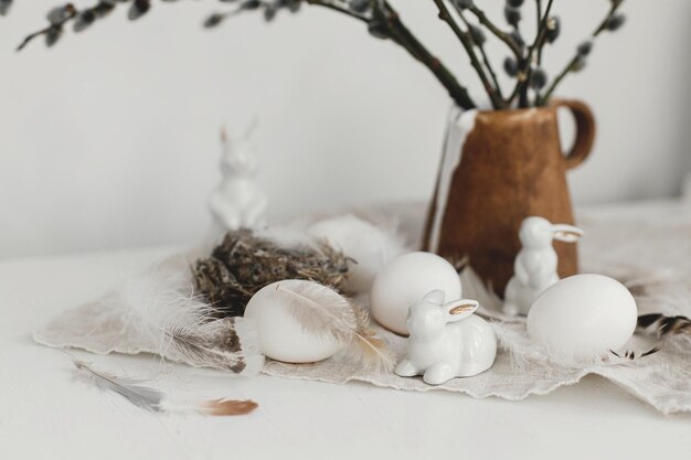 Happy Easter Natural eggs bunny figurines feathers nest willow branches in vase on table