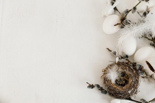 Happy Easter Natural eggs feathers nest willow branches border on white wood Rustic flat lay