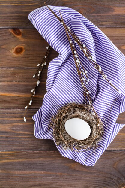 Happy easter. One white chicken egg in a bird's nest and willow branches on a wooden table. Rustic style. Copy space.