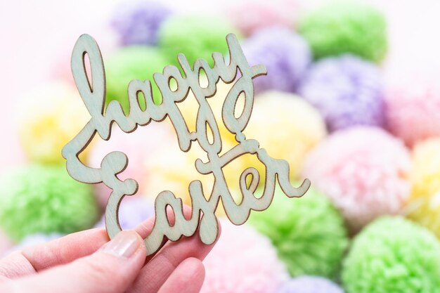 Happy Easter sign and pastel color pom poms on a pink background.