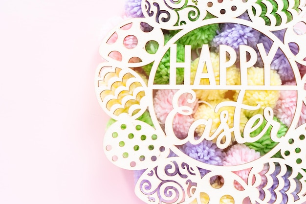 Happy Easter sign and pastel color pom poms on a pink background.