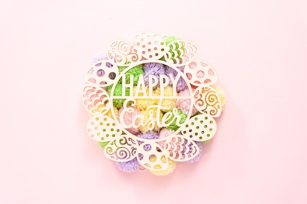 Happy Easter sign and pastel color pom poms on a pink background.