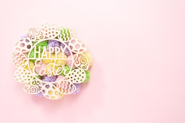 Happy Easter sign and pastel color pom poms on a pink background.