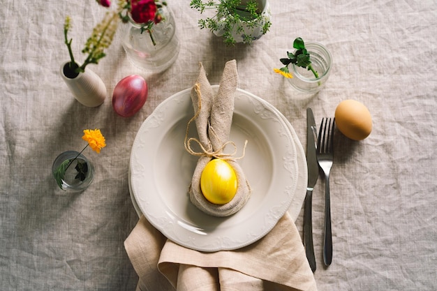 Happy Easter Stylish easter eggs on a napkin with spring flowers on white wooden background Table setting The concept of a happy Easter holiday