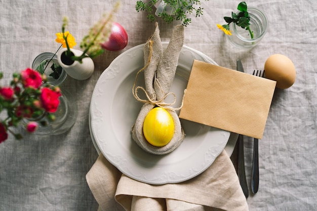 Happy Easter Stylish easter eggs on a napkin with spring flowers on white wooden background Table setting The concept of a happy Easter holiday