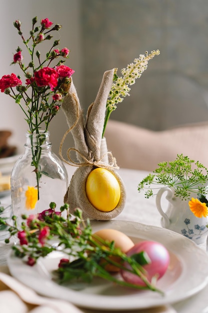 Happy Easter Stylish easter eggs on a napkin with spring flowers on white wooden background Table setting The concept of a happy Easter holiday