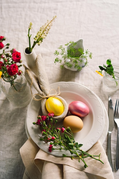 Happy Easter Stylish easter eggs on a napkin with spring flowers on white wooden background Table setting The concept of a happy Easter holiday