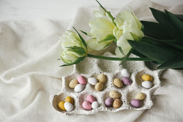 Happy Easter Stylish easter eggs in tray and tulips on rustic table flat lay Natural candy chocolate eggs with spring flowers Easter hunt space for text