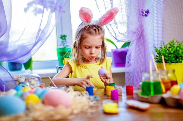 Happy easter woman in bunny ears painting eggs, small child at home. spring holiday