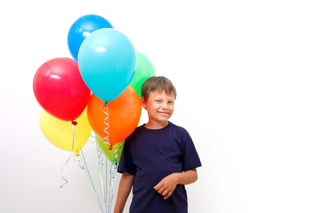 明るいカラフルな風船の腕を持つ幸せな8歳の男の子は誕生日を祝います。