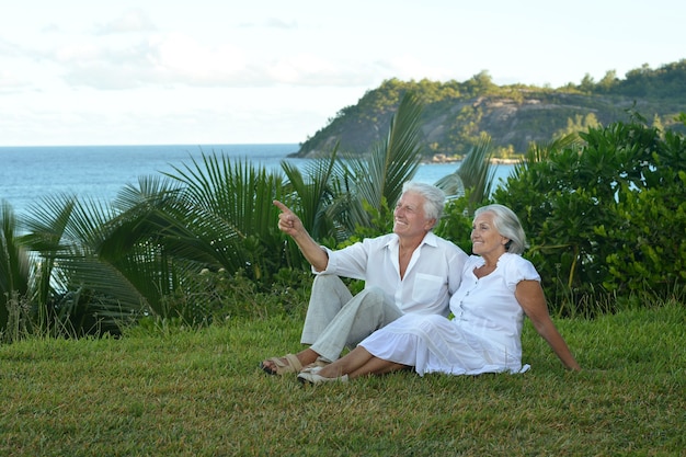 Счастливая пожилая пара отдыхает на тропическом пляже, мужчина показывает рукой