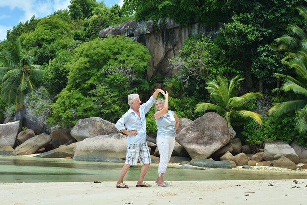 Happy elderly couple on sandy beach near tropical resort