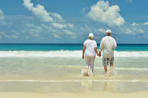 Felice coppia di anziani che cammina sulla spiaggia tropicale