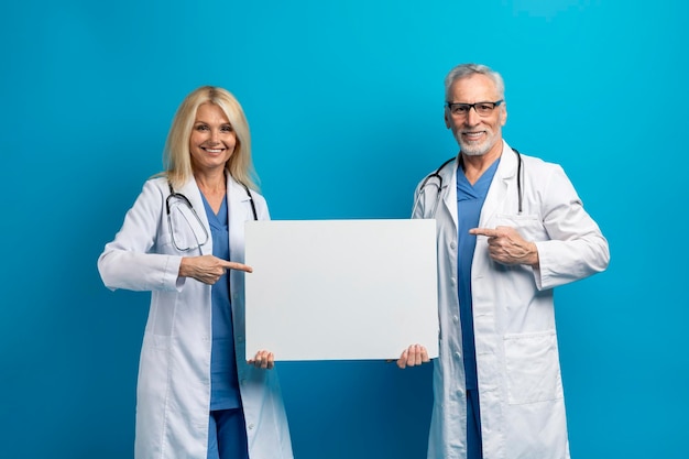 Happy elderly doctors showing white blank placard for advertisement