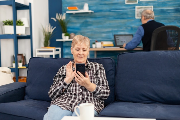 Happy elderly lady waving at smartphone during video call