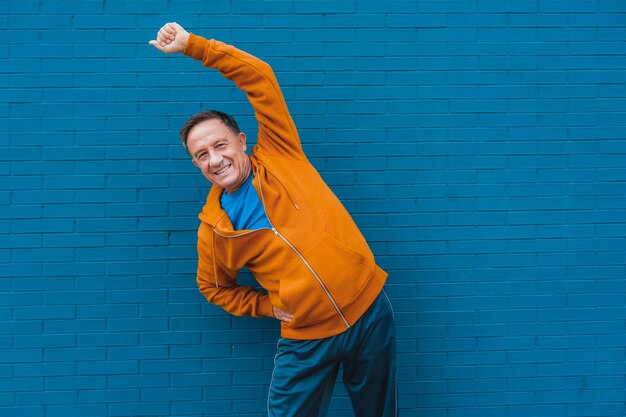 Happy elderly male stretching in front of a blue wall